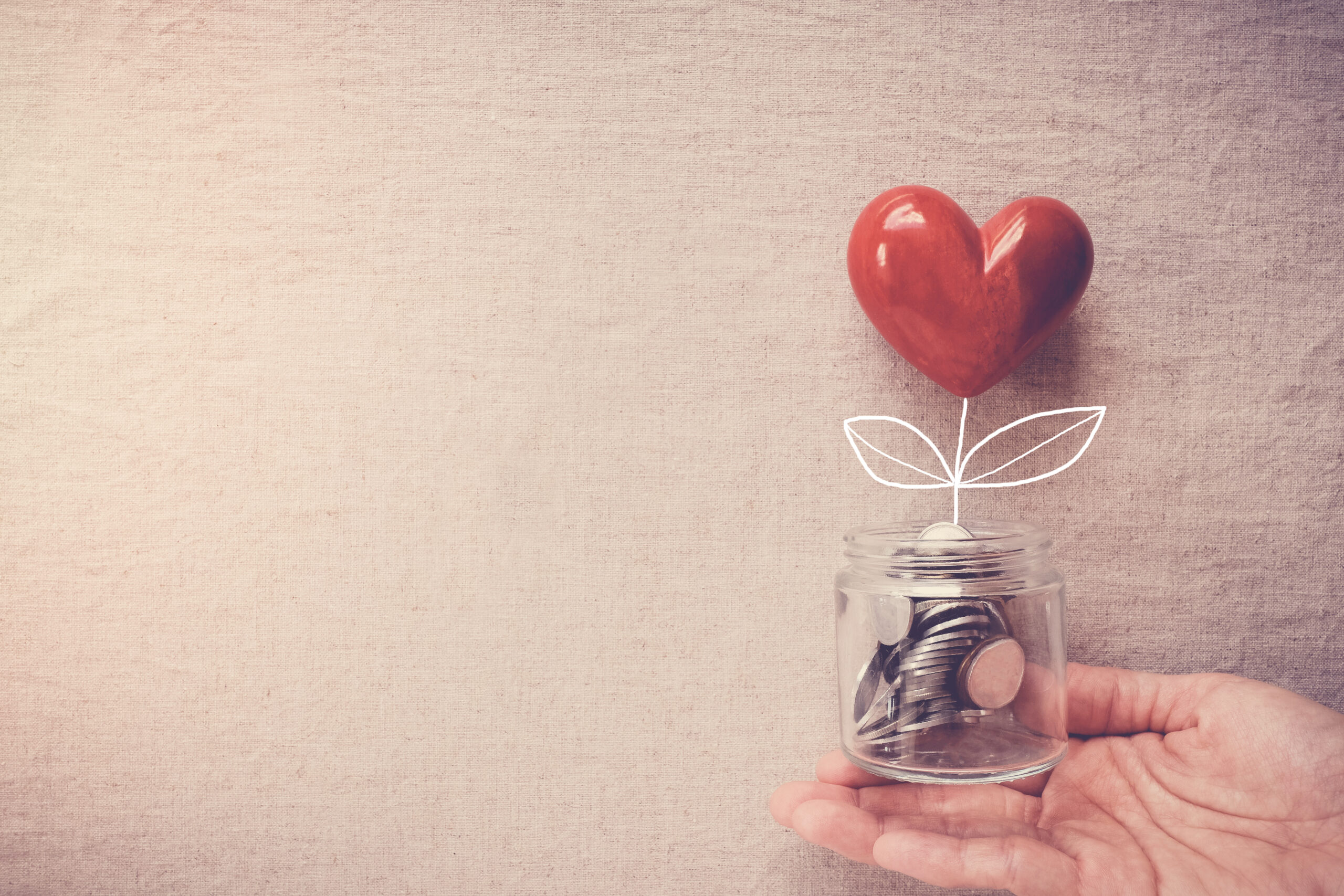 Hand holding a jar of heart tree growing on money coins,charity, social responsible business and donation, fundraising, relief plan concept